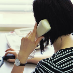 En kvinna sitter och pratar i telefonen vid en dator.