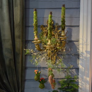En trearmad väggkandelaber som har dekorerats med mossa, kvistar och kottar.