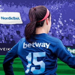 En kvinna på en fotbollsplan fylld med spelbolagsreklam.