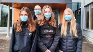 Tia Utunen, Nelli Mäkelä och Oona Nissinen går i språkbadsklassen i åk 8. De tycker det är bra att använda munskydd även om det är lite obekvämt. I bakgrunden syns rektor Jouni Piippo. Tre skolelever står framför ingången till Nickby hjärta. Bakom dem syns en äldre man, skolans rektor. Alla har munskydd på sig.