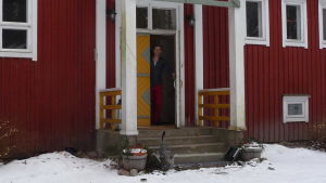 Jon hälsar välkommen till Villa Christine. Jon LIndström vid ytterdörren till en gammal skola, numera hem och kursgård. Vinter