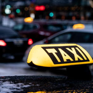 En gul taxi-skylt på ett biltak, i bakgrunden fler taxibilar.