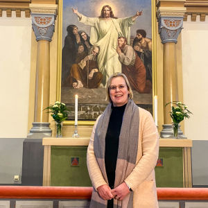 En leende kvinna står framför altaret i en kyrka.