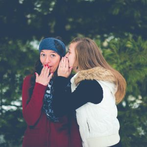 Tyttö kuiskaa toiselle tytölle jotain