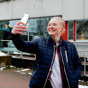 Nadine Baarman poserar i selfie-ställning utanför Yles studiohus.