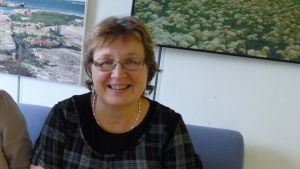 Eva-Stina Hellbom har förtroende för Rinne och anser att oppositionen från dag ett har försökt fälla Rinne och regeringen. Eva-Stina Hellbom sitter och ler mot kameran.