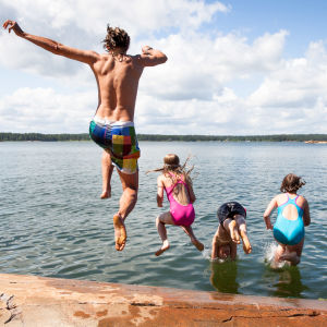 En kille och några barn hoppar i vattnet från en klippa.