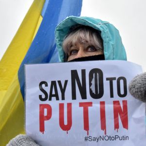 En kvinna håller i en skylt med texten "Say no to Putin". Ukrainas flagga syns i bakgrunden.