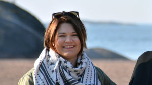 Jennika Friman är glad över att många kan dela på ansvaret. Kvinna med mörkt hår och solglasögon uppe på hjässan ler mot kameran. Klippa, strandoch hav syns i bakgrunden.