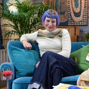 En kvinna som sitter i en soffa. Kvinnan är textilexperten Leili Mänder som jobbar med att sprida kunskap om textilvård och hållbarhet och som driver kontot @lagningsaktivisterna på Instagram.