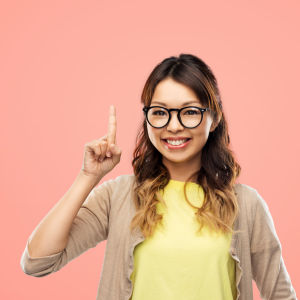 En ung kvinna med glasögon håller upp sitt ena pekfinger. 