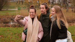 Tre ungdomar, en pojke och två flickor, i en grupp som tar en selfie.