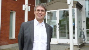 Juha-Pekka Isotupa Sjundeås kommundirektör Juha-Pekka Isotupa står leende i kostym framför kommungården.