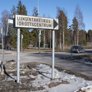En skylt där det står idrottscentrum. Skylten står vid en korsning av en gång- och cykelväg och en bilväg.
