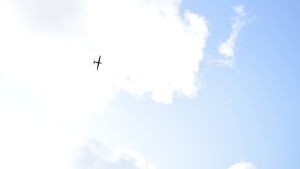 Från marken såg drönaren ut som ett litet flygplan. En drönade i luften, fotograferat från marken. Drönaren är en svart siluett mot molnen.