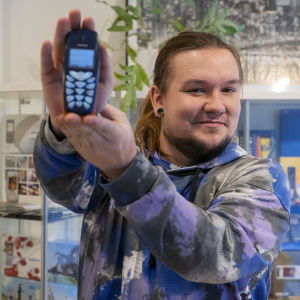 En man i 20-årsåldern håller i en gammal Nokia-telefon och tittar in i kameran.