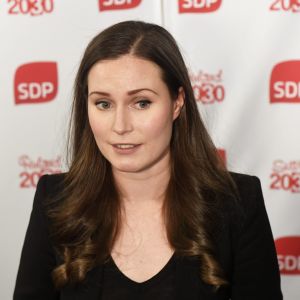 SDP:s Sanna Marin. Hon står framför ett lakan med texten SDP.