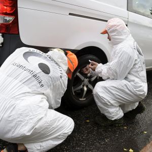 Två personer i vita overaller kontrollerar däcket på en paketbil.
