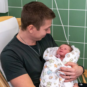 Mysig stund för far och son Lönnqvist. Lucas Lönnqvist sitter i gungstolen och har bebisen i famnen. Bebisen tittar på pappan som ler.
