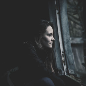 En ung kvinna tittar ut genom ett fönster och ser bekymrad ut.