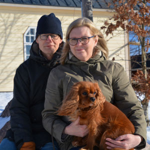 Paret Andersson och deras hund sitter på en sten utanför det gula bönehuset.