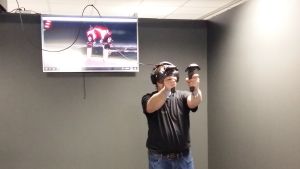 Juuso Salmi räddar världen i ett VR-spel. En man med VR-glasögon spelar ett spel där rymdvarelser ska stoppas.