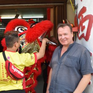 Petri Karjalainen låter sig inte störas av en man som i en lejonmask offrar vid ett litet altare. Karjalainen upplever att den kinesiska minoritetens ritualer är fascinerande. En man i kortärmad skjorta tittar mot kameran. En annan offrar vid ett altare