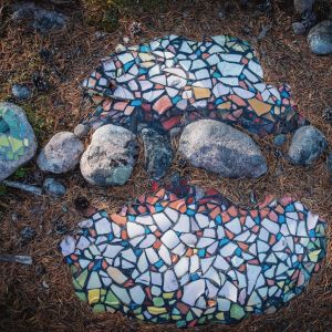Värikkäitä mosaaikinpaloja kiinnitettynä kiviin metsässä