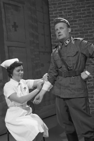 Päivystävä kersantti Paavo Einiö huoltojoukkojen hoivassa Iskelmäkarusellin armeijajaksossa. Paavo Einiö kersantin asussa sairaanhoitajan hoidettavana Iskelmäkarusellissa 1962.