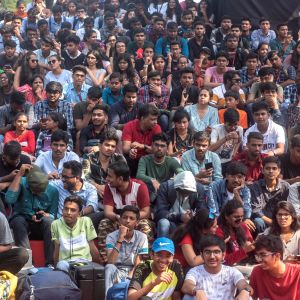 Iso joukko intialaisia opiskelijoita istuu maassa. Useimmilla t-paita, enemmän miehiä kuin naisia. 