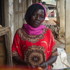 Den ugandiska kvinnan Ester Nansibirwa ser mot kameran, iklädd röda kläder och en lila sjal.