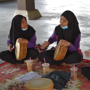 Tre kvinnor i burka sitter på en matta på golvet och spelar handtrumma.