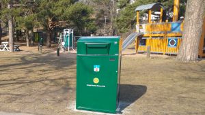 Ett av de smarta sopkärlen står vid Lejonparken i Hangö. Ett grönt smart sopkärl står invid en lekpark.