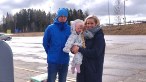 Antti Laitinen och Anna-Maija Tenojoki med dottern Ilona Laitinen. En man, en kvinna och ett barn på en parkeringsplats.
