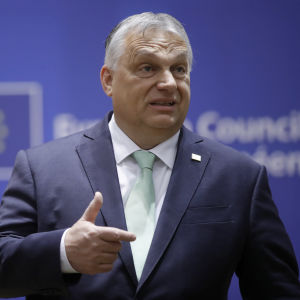Viktor Orbán puhuu ja elehtii sinisen EU-lippuisen taustan edessä.