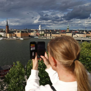 Nuori nainen ottaa kuvaa älypuhelimella Tukholmasta Södermalmin rantatörmältä heinäkuussa 2022.