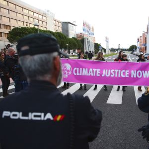 Tre poliser står med ryggen mot kameran och ser på när klimataktivister demonstrerar på en gata.