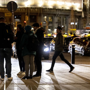 Ryhmä ihmisiä seisoo keskustellen, taustalla näkyy taksiasemalla odottavia takseja.