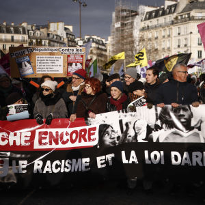 Demonstranter bär en banderoll med fransk text: Marche Encore (Marscherar igen) och Contre le racisme et la loi Darmanin (Mot rasism och Darmanin-lagen).