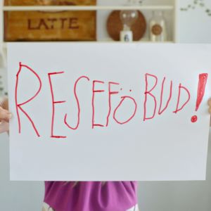 Ett barn håller upp ett stort pappersark med texten "RESEFÖBUD!".