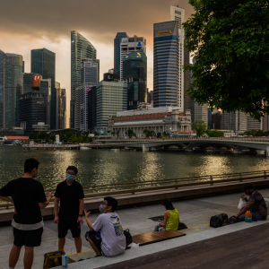 Ihmisiä veden äärellä Singaporessa. Taustalla pilvenpiirtäjiä ilta-auringossa.