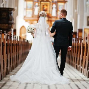 Ett brudpar går med ryggen till kameran längs mittgången i en kyrka. 