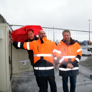 Hangö hamns vd Anders Ahlvik knäpper på det gröna ljuset. Till höger Björn Peltonen och till vänster Roger Nordlund från Sandö Betong. Tre män, två har reflexjackor, en håller i ett paraply. En av männen i reflexjacka trycker på en knapp.