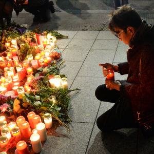 En ung man tänder ett ljus till minnet av terroroffren i Berlin. mannen håller på att lägga ner ljuset vid ett hav av blommor och ljus som lämnats av andra Berlinbor.