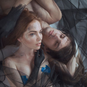 Taiteellinen kaksoismuotokuva miehestä ja naisesta makaamassa mustan harson keskellä.