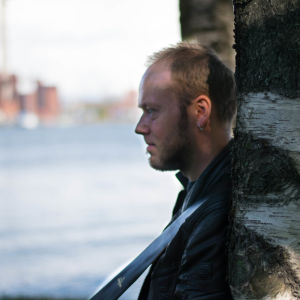 Mikael Grönroos har på senaste tid snöat in sig på synthwave med åttiotalsstuk. Mikael grönroos i profil lutad mot Björk på Tjärholmen med vatten och fabriker i bakgrunden.