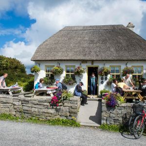 Här ser vi en tvättäkta irländsk pub i Arainn på Aran-öarna på Irland. En pittoresk irländsk pub omgärdad av stenmur på landsbygden med folk på terrassen.