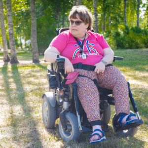 En kvinna i en rullstol på en gräsmatta. Vädret är soligt. Kvinnan tittar bort från kameran och ser allvarsam ut.