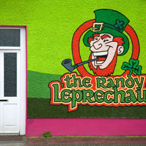 Den kåta gnomen pryder en Bed and breakfast-vägg på Irland. Fasad över ett Bed and breakfast på irland med grön vägg och tecknad Leprechaun och stor text The randy leprechaun.