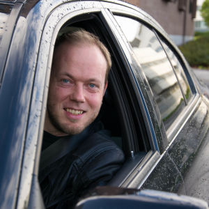 Mikael Grönroos sticker leende huvudet ut ur bilens sidofönster i duggregn.